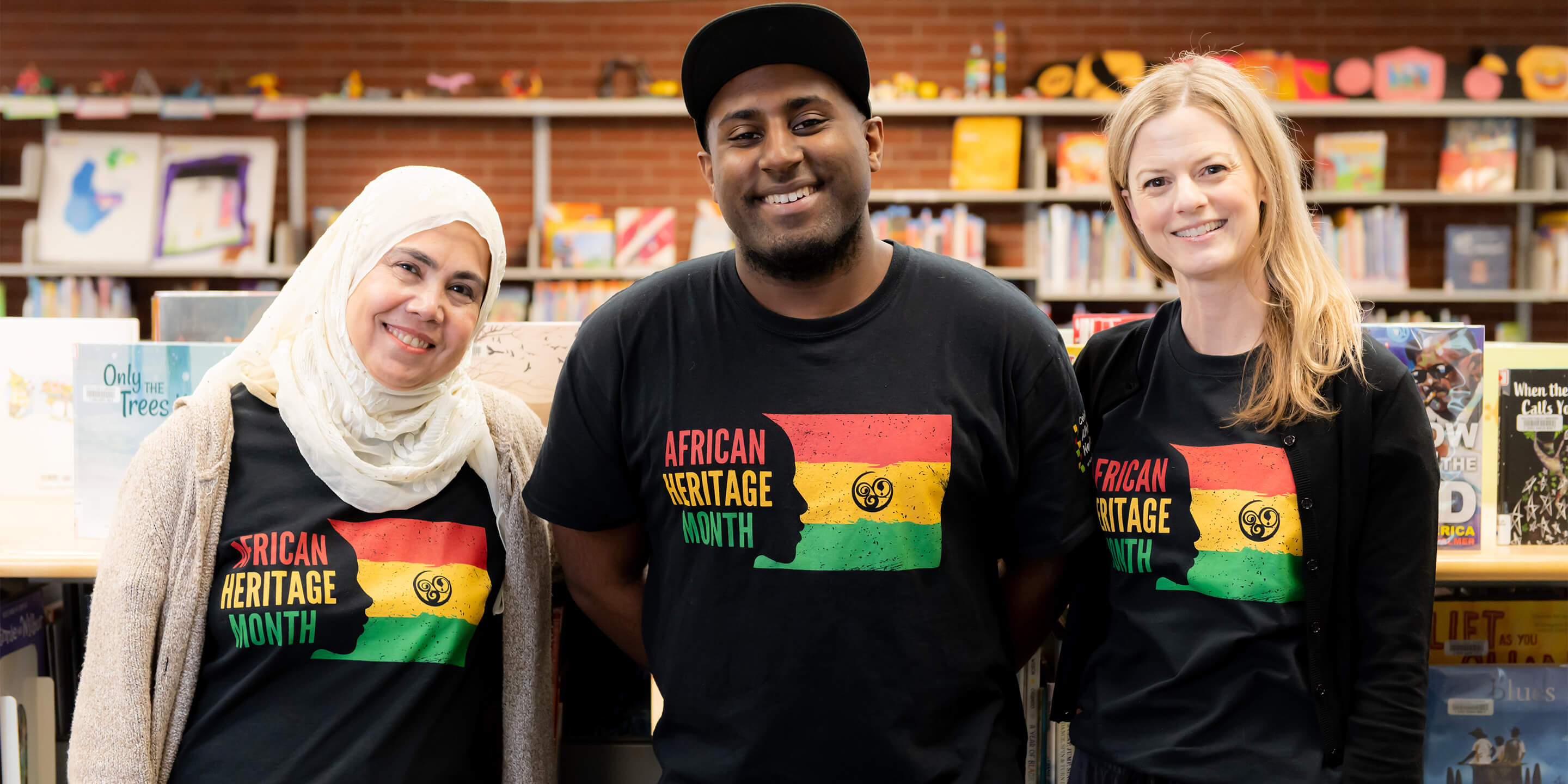 3 staff wearing african heritage month t-shirts smiling to cameara.